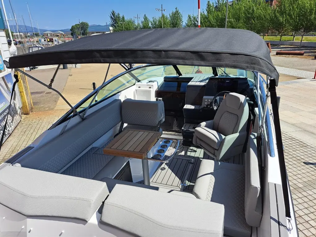 Interior of a sleek boat featuring gray cushioned seating, a wooden table, and modern control panel under a black canopy.